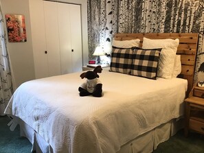 A neatly made bed with a checkered pillow, a small bedside table with a lamp, and a wall clock. - Yes it's summer, but Fall is only a few months away!  Book now! (Angel Fire)