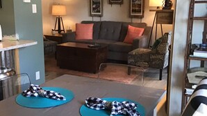 A living room with a sofa, armchairs, a coffee table, and a dining table with placemats.