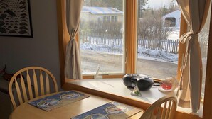 Un comedor con una mesa y sillas de madera, una ventana con cortinas y vistas a un paisaje nevado.