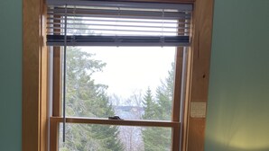 Una habitación con ventana, una cama con almohada estampada, una lámpara y una mesita de noche de madera.