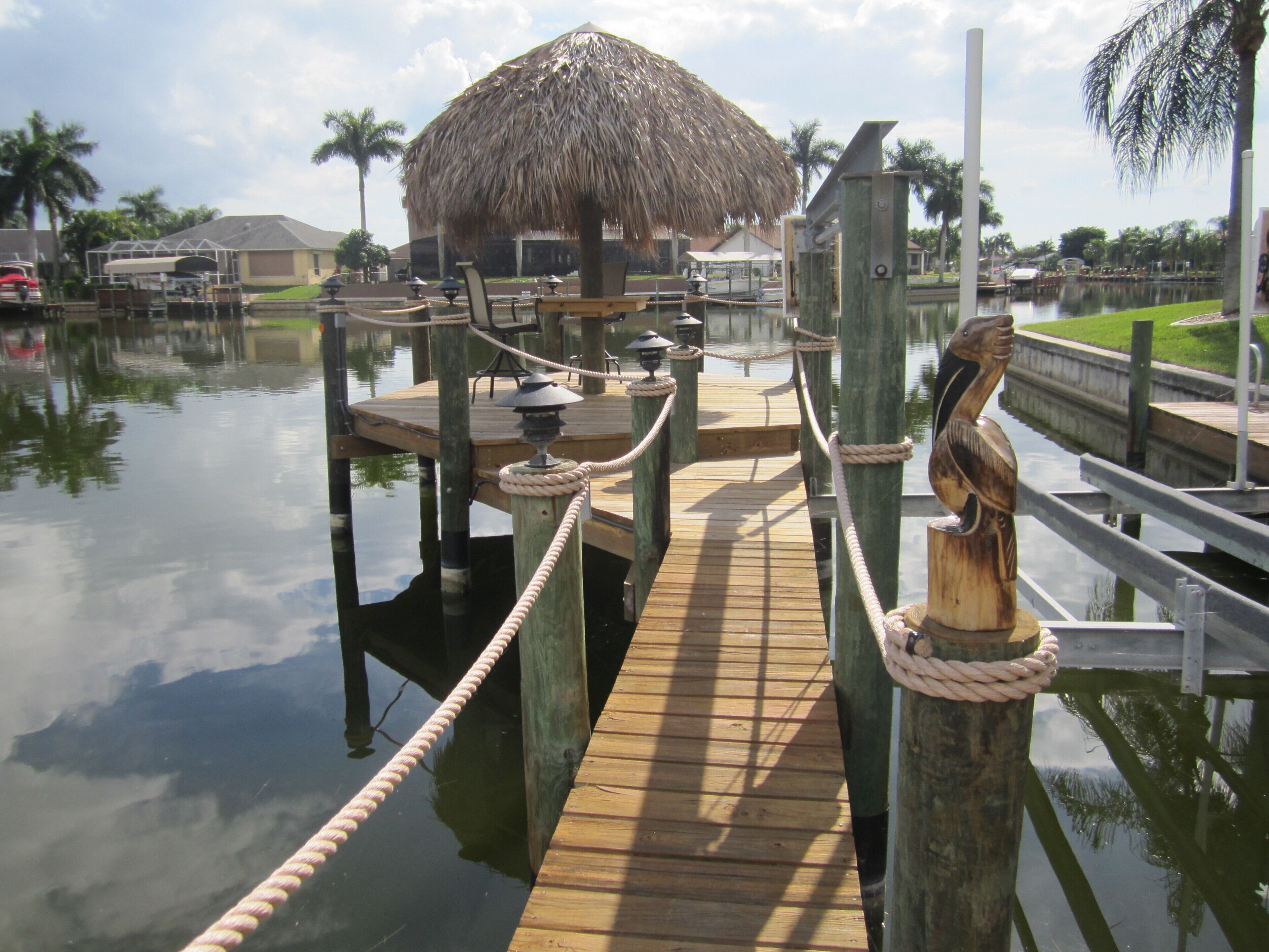 A wooden dock with a rope barrier, a thatched-roof structure, and a wooden statue.
