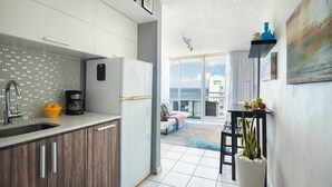 A modern kitchen with a large window, a dining area with a table and chairs, and a balcony with a view. - Ocean View  19 floor  STUDIO Apt In the Condado Area NO PARKING (San Juan)