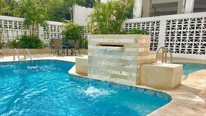 A swimming pool with a waterfall feature, surrounded by a white fence and palm trees. - Ocean View  19 floor  STUDIO Apt In the Condado Area NO PARKING (San Juan)