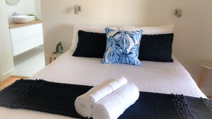 Un lit bien fait, avec une literie blanche et noire, un oreiller bleu et blanc, et une serviette blanche enroulée sur un plaid bleu foncé.
