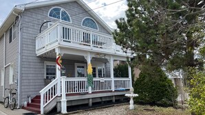 A two-story house with a front porch, a small garden, and a bicycle parked outside. -  Cozy 2 bedroom Apartment Half block to beach, Front deck, Fenced in backyard. (Ship Bottom)