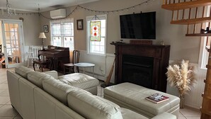 A living room with a beige sofa, a small round table, a fireplace, and a television mounted above it. -  Cozy 2 bedroom Apartment Half block to beach, Front deck, Fenced in backyard. (Ship Bottom)