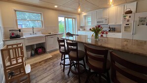 A modern kitchen with white cabinets, a central island, wooden chairs, and pendant lighting. -  Cozy 2 bedroom Apartment Half block to beach, Front deck, Fenced in backyard. (Ship Bottom)