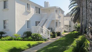 A two-story residential building with a white exterior, a central staircase, and a well-maintained lawn. - Newly refreshed  Beach Apartment..Steps to the sand! (San Diego)