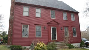 A two-story red house with a brick chimney, multiple windows, and a front door. - Charming 5 bedroom Easton Point colonial with honeymoon suite on 3rd floor (Middletown)