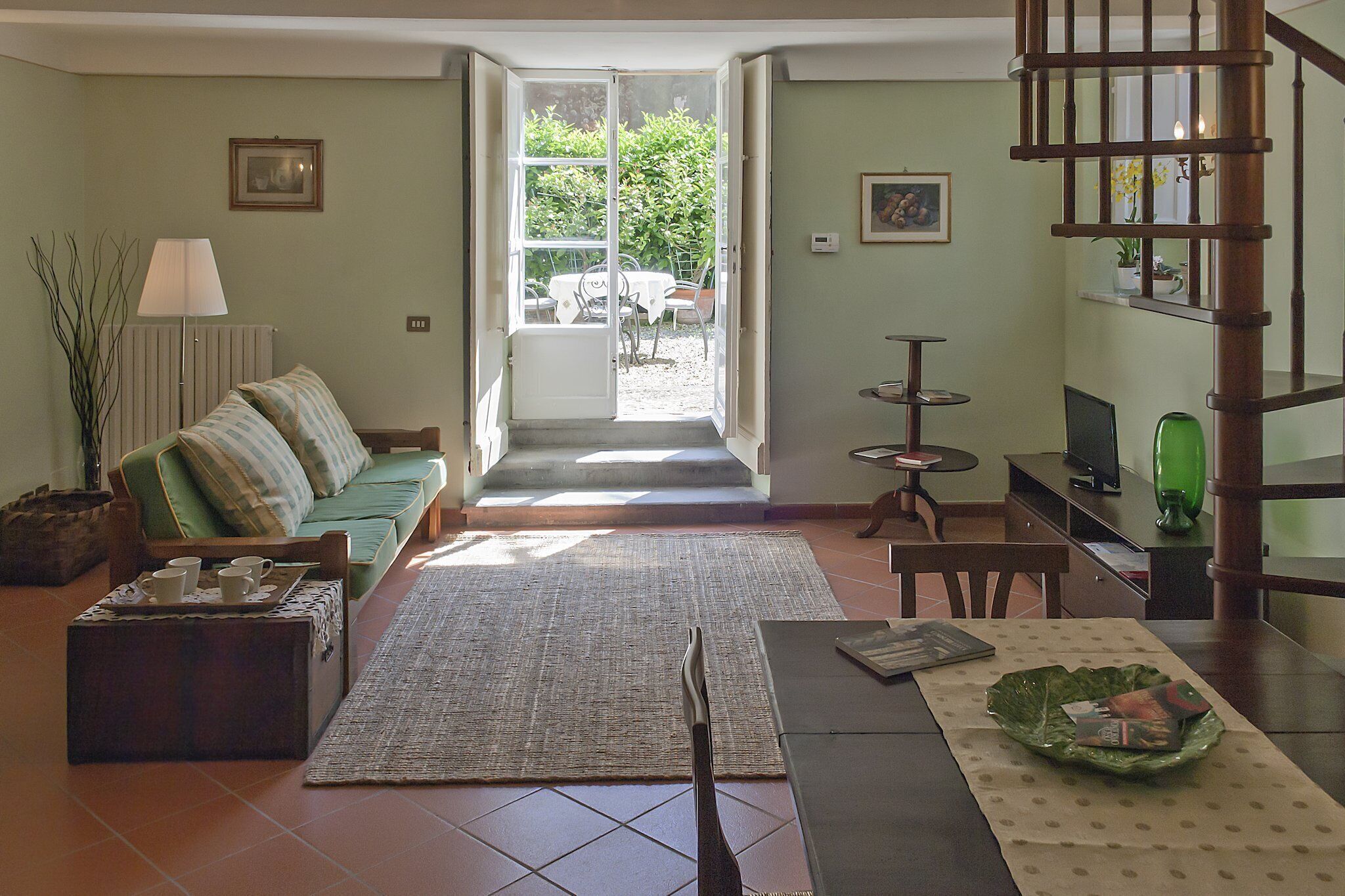 Una sala de estar con un sofá, una mesa de centro y un comedor con mesa y sillas. Hay una escalera que conduce a un nivel superior.