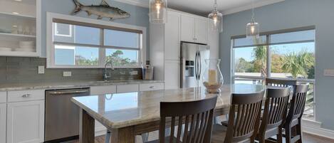 A modern kitchen with white cabinets, a stainless steel refrigerator, and a large island with chairs.