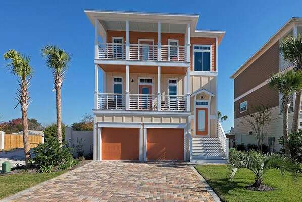 A multi-story residential building with a two-car garage, a balcony on the upper floor, and a well-maintained lawn with palm trees. - Close to beach! Golf Cart! Private Pool, Gulf Views, Bikes (Miramar Beach)