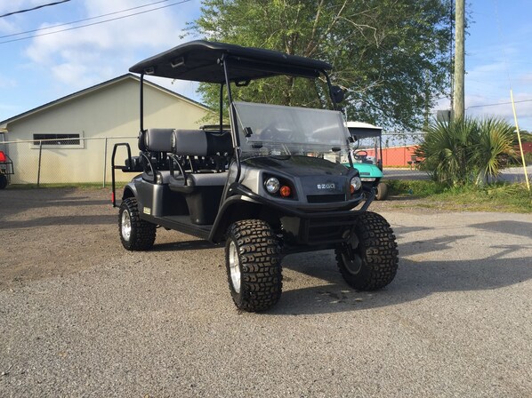 A golf cart parked on a gravel surface with a building in the background.
