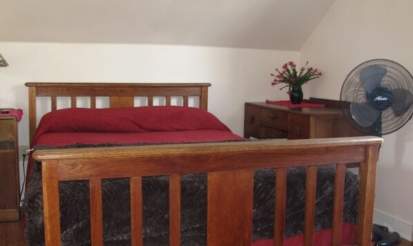 A bedroom with a wooden bed, a small bedside table, a dresser, a fan, and a vase with flowers. - Hill Country getaway - Next to Hamilton Pool (Round Mountain)