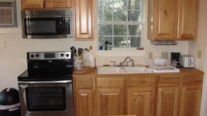 A kitchen with wooden cabinets, a stainless steel microwave, an oven, a sink, and a window with a view of trees.