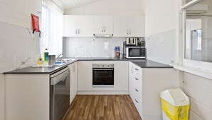 Una cocina compacta con armarios blancos, horno empotrado, microondas y lavavajillas.