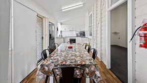Un comedor con una mesa larga, sillas y un mantel estampado. Hay un extintor de incendios montado en la pared.