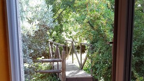 A view through a window of a wooden deck leading to a garden area with a wooden bridge and a stone path.