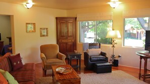 A cozy living room with a striped sofa, armchairs, a wooden coffee table, and a large window with a view of trees.