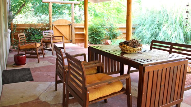 A covered patio with wooden furniture and a table set for dining.