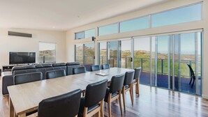 Una amplia sala de conferencias con una larga mesa y sillas, un televisor y ventanas grandes que ofrecen vistas al paisaje.
