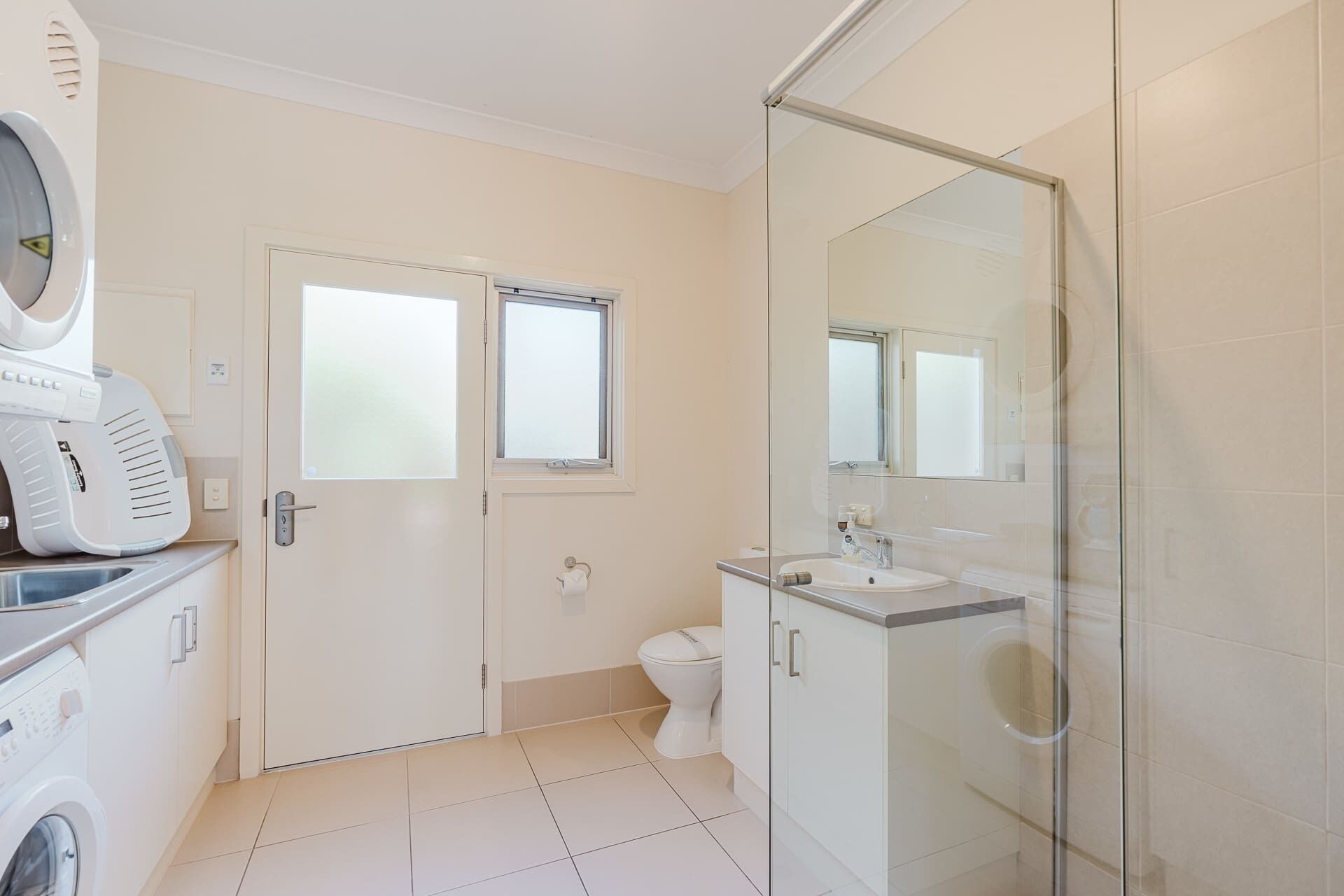Een moderne badkamer met een glazen douchecabine, een toilet en een wasmachine.