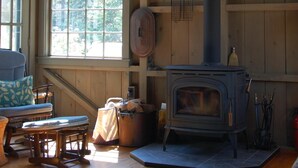 A cozy cabin interior with a wood-burning stove, large windows, and a wooden interior. - Prud'homme Cottage: bright, private architectural cottage on Mitchell Cove (Bernard)