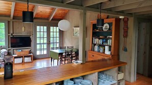 A rustic kitchen with wooden beams, a wooden dining table, chairs, a coffee maker, and a bookshelf. - Prud'homme Cottage: bright, private architectural cottage on Mitchell Cove (Bernard)