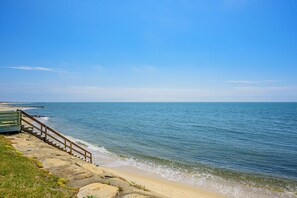 A coastal view with a wooden staircase leading down to the beach, clear skies, and calm sea.
