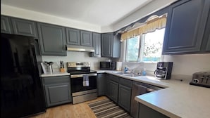 A modern kitchen with grey cabinets, a black refrigerator, a microwave, a stove, and a coffee maker.