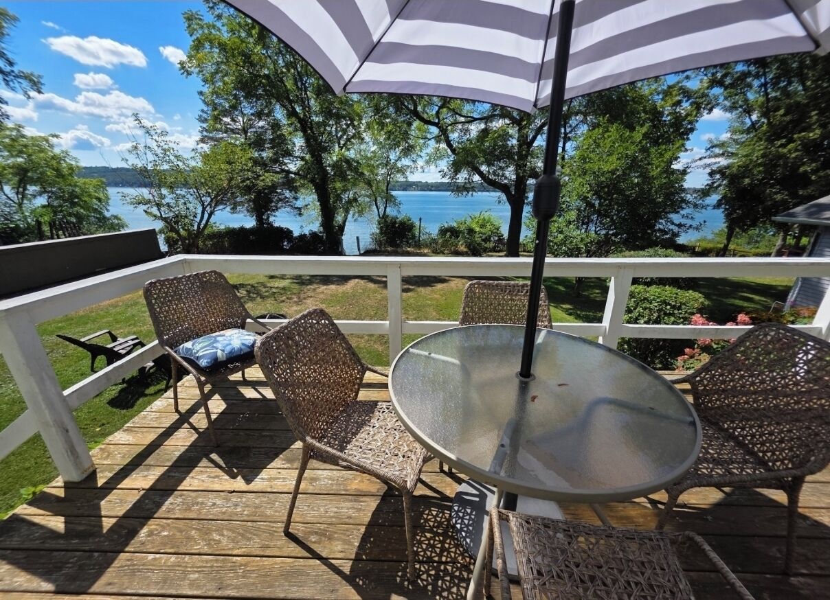Une terrasse en bois avec des chaises en osier et une table en verre, donnant sur un lac.