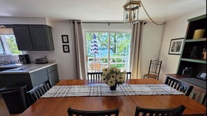 A dining area with a wooden table, black chairs, a vase with flowers, and a view through a glass door.