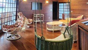 Una habitación amplia con pisos de madera, una silla colgante y un televisor en la pared.