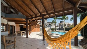 Un espacio al aire libre cubierto con piscina, una hamaca y un patio con mesas y sillas.
