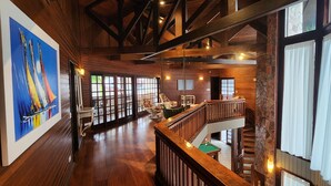 Un interior espacioso con vigas de madera, una mesa de billar y una escalera que lleva a un nivel superior.