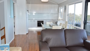 Une cuisine moderne avec des meubles blancs, un coin repas doté d’une table et de chaises en verre, et une grande fenêtre offrant une vue sur l’extérieur.