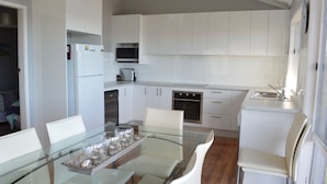 Une cuisine moderne avec des meubles blancs, un four à micro-ondes, un réfrigérateur et un coin repas comprenant une table et des chaises en verre.