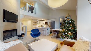 Un salon moderne avec une cheminée, un coin repas et une cuisine. On aperçoit un sapin de Noël au fond.