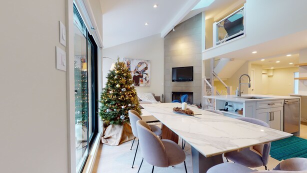 Une cuisine moderne dotée d’un four encastré, un coin repas avec une table en marbre et un sapin de Noël.