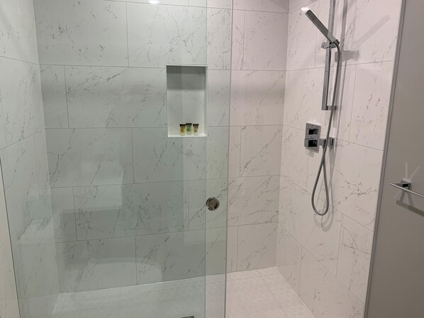 Un espace douche moderne doté d’une porte en verre, d’un pommeau de douche à main et d’une étagère pour les articles de toilette.