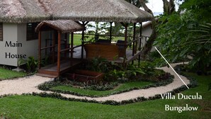 Uma villa com telhado de palha, varanda coberta e um jardim com caminho de cascalho.