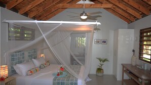 Um quarto com cama de dossel, ventilador de teto, mesa de cabeceira com abajur e janela com vista para o verde.