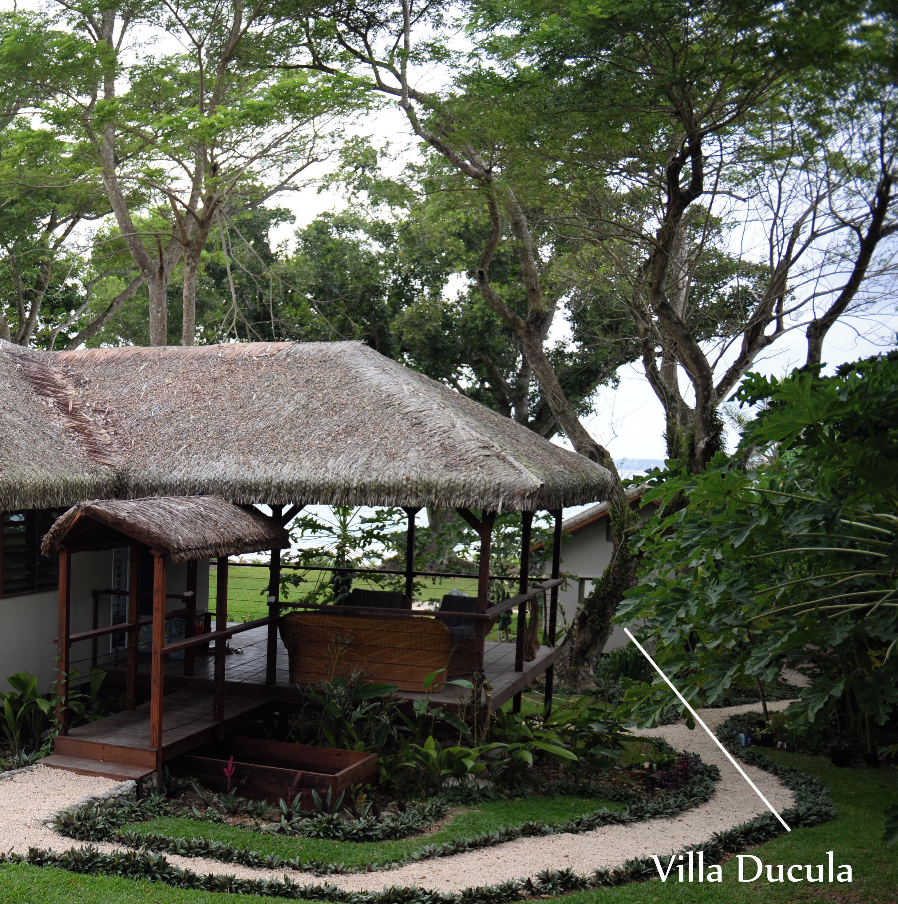 Una villa con tetto di paglia, un portico coperto e un giardino con vialetto in ghiaia.