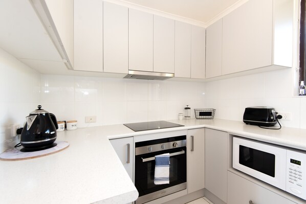 A modern kitchen with white cabinetry, a black kettle, a toaster, and an oven. - 1 Commodore Batehaven Premium Beachfront Bliss (Batehaven)