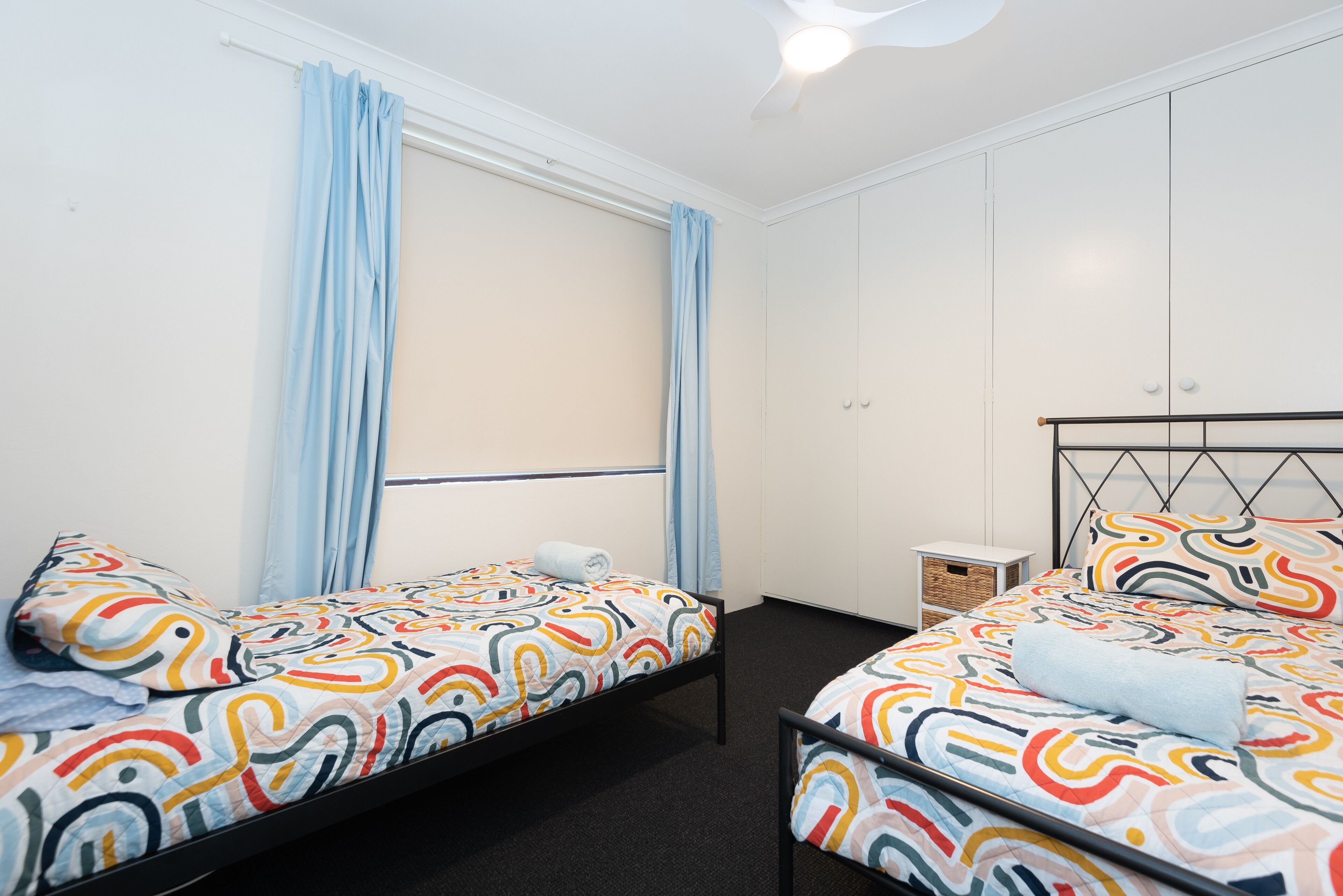 Une chambre double avec deux lits, une petite table de chevet, une armoire et une fenêtre avec des rideaux.