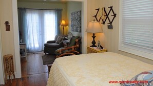 A bedroom with a bed, a chair, a lamp, and a window with blinds. - Our 'Someday' Cottage - Second Row (Surf City)