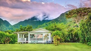 A two-story house with a balcony, surrounded by lush greenery and mountains in the background. - Hanalei Bay, ocean view bungalow. Steps to sand,1B/1BA Local style, romantic! (Hanalei)