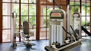 A gym with exercise equipment, large windows, and a view of greenery outside.