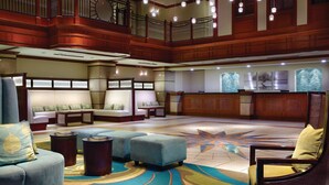 A spacious lobby with a high ceiling, a central seating area with sofas and ottomans, a reception desk, and a decorative star-patterned floor.