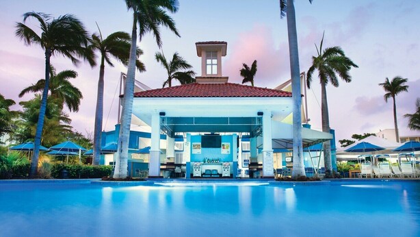 A resort with a large pool, palm trees, and a building with a red-tiled roof.